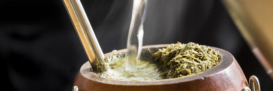 Hot water being poured into an earthy mug with yerba mate leaves to brew a cup.