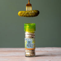 Dill Pickle Sea Salt Seasoning on table with dill pickle in fork above it