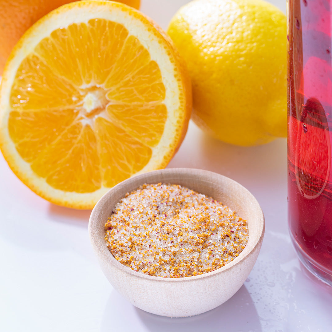 Florida Sunshine Sugar in white bowl surrounded by oranges cut in half and a pitcher of pinkish red tea