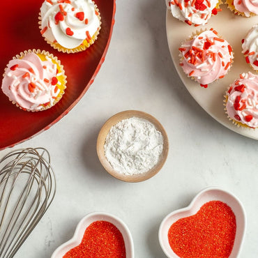 Lavender Lemon Monk Fruit Sweetener in wood bowl surrounded by valentine's day cupcakes and heart bowls with red sugar in