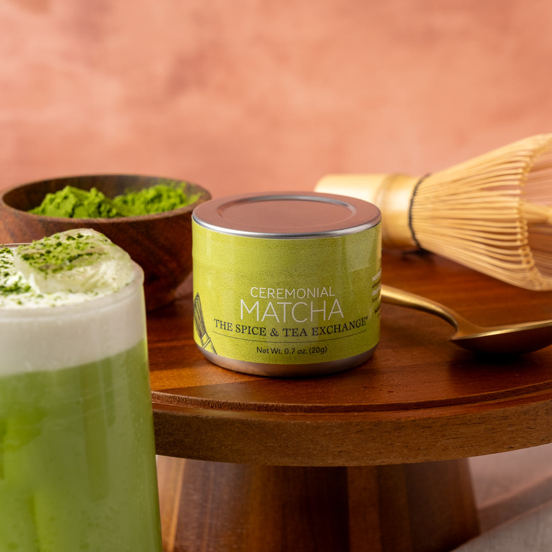 Ceremonial Matcha Tea (0.7 oz tin) - matcha powder and whisk next to iced matcha latte